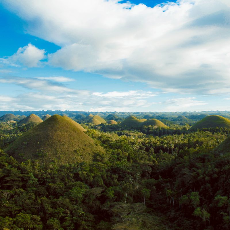 The Chocolate Hills of Bohol under a wide cloudy sky.