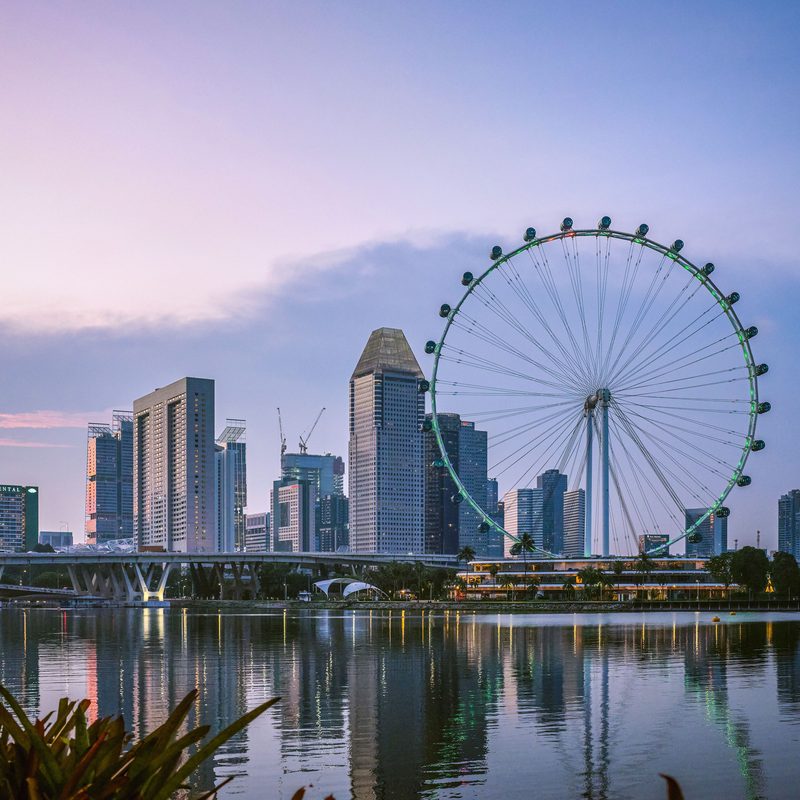 The Singapore Flyer and the Marina Bay skyline at dusk, reflected in the water.